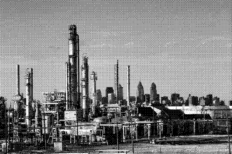Distillation towers of an oil refinery, with a city skyline behind them
